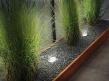 Recessed stainless steel LED floor lights illuminate gravel bed with green grasses, modern energy-saving lighting