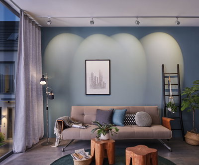 Modernes Wohnzimmer mit beigem Sofa, blauen Kissen, Holzhockern und dimmbaren Deckenstrahlern an blauer Wand