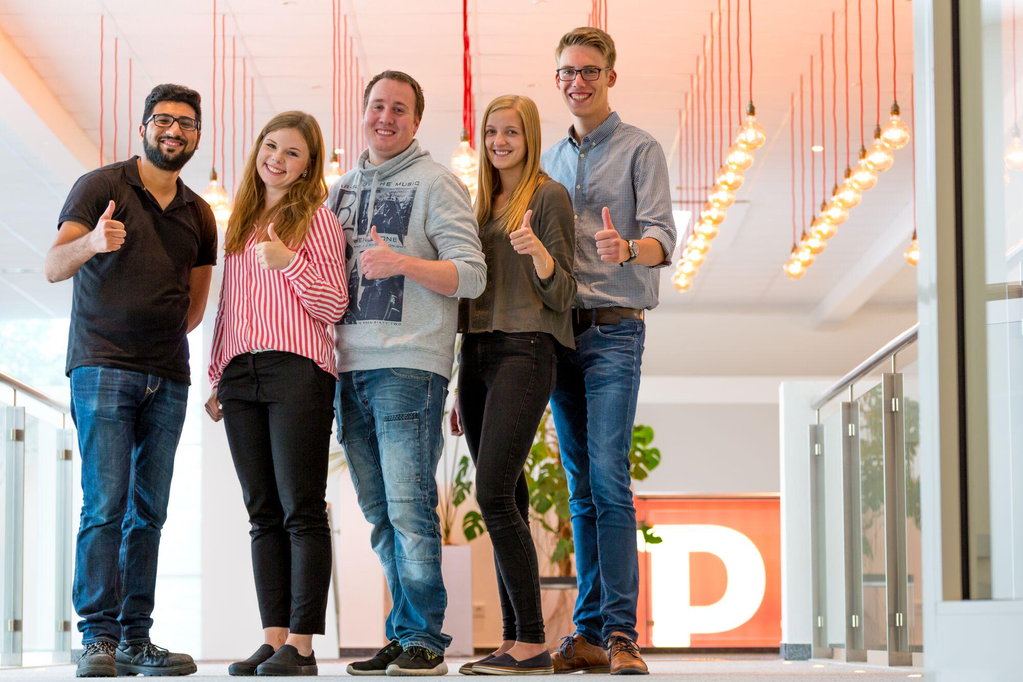 Cinq jeunes dans un bureau moderne montrent le pouce levé sous des lumières LED chaudes.