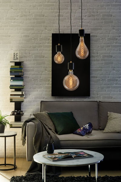 Drie LED-filamentlampen met warm goud licht boven een grijze bank en witte bakstenen muur.
