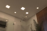 Moderne badkamer met vierkante warmwitte LED-plafondlampen en glazen douche met regendouchekop