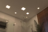Modernes Badezimmer mit quadratischen LED-Deckenleuchten in warmweiß und Glasdusche mit Regenduschkopf