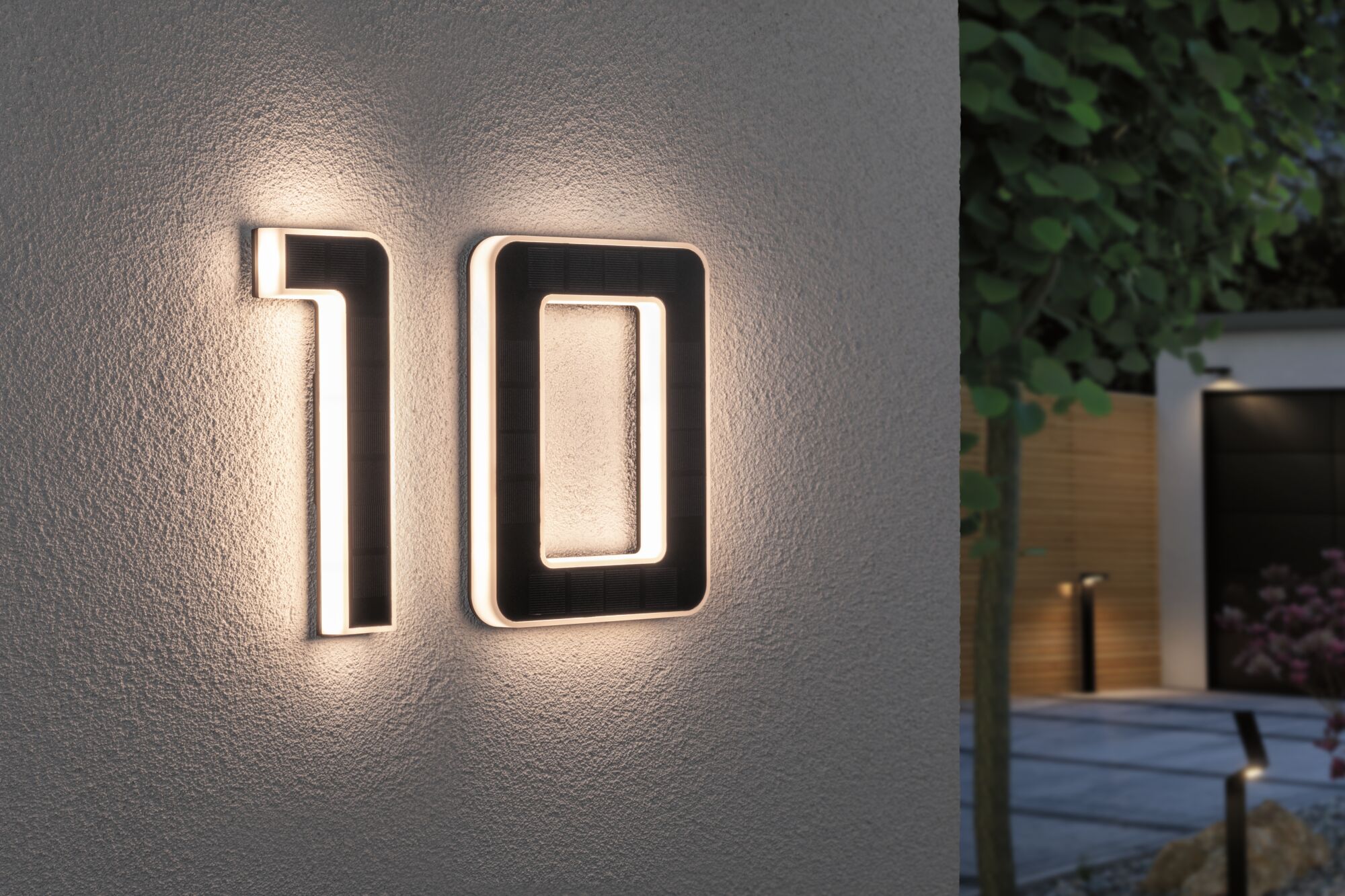Huisnummer 10 van zwart materiaal met geïntegreerde LED-verlichting aan witte buitenmuur