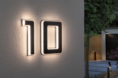 Huisnummer 10 van zwart materiaal met geïntegreerde LED-verlichting aan witte buitenmuur