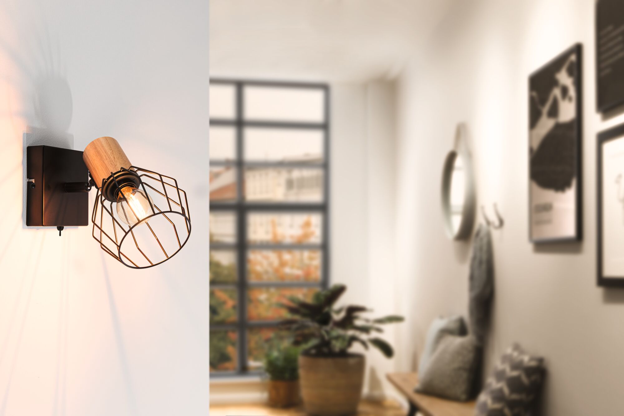 Wall lamp with wood and black metal cage, warm light in modern living room with window and plants.
