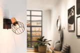 Wall lamp with wood and black metal cage, warm light in modern living room with window and plants.