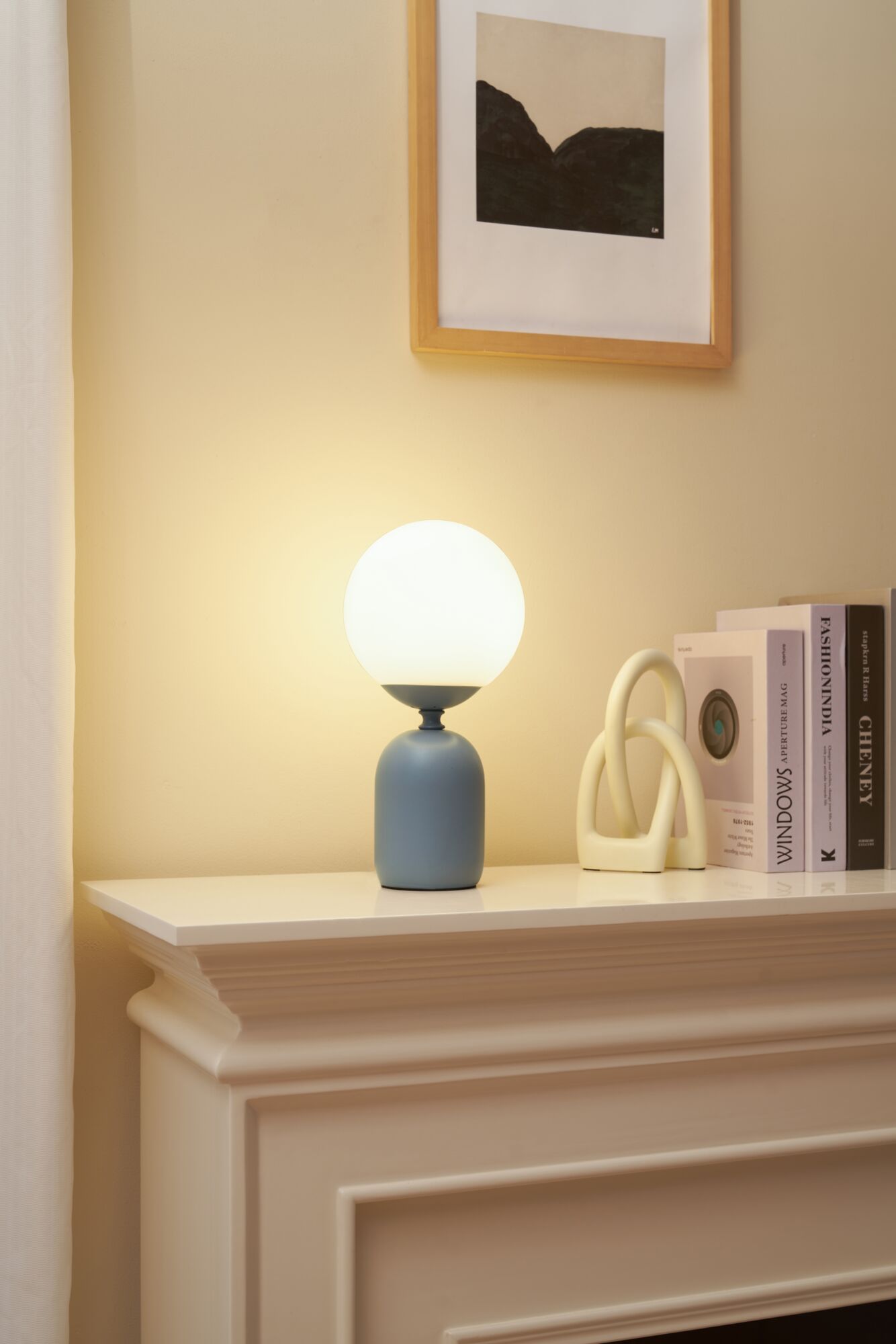 Moderne tafellamp met matte blauwe keramische voet en witte glazen bol kap op schoorsteenmantel.