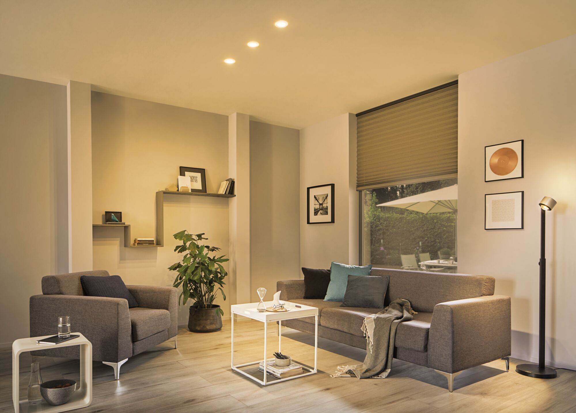 Wohnzimmer mit warmweißem LED-Deckenlicht, grauem Sofa und Sessel, moderner Stehleuchte und Holzfußboden