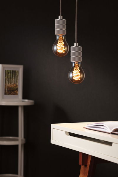 Zwei hängende Glühbirnen mit warmem Licht und grauen Fassungen vor dunklem Hintergrund im modernen Arbeitszimmer.