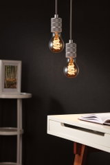 Zwei hängende Glühbirnen mit warmem Licht und grauen Fassungen vor dunklem Hintergrund im modernen Arbeitszimmer.