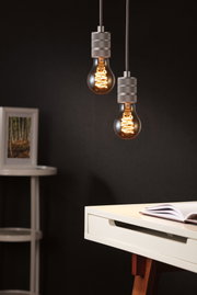 Zwei hängende Glühbirnen mit warmem Licht und grauen Fassungen vor dunklem Hintergrund im modernen Arbeitszimmer.