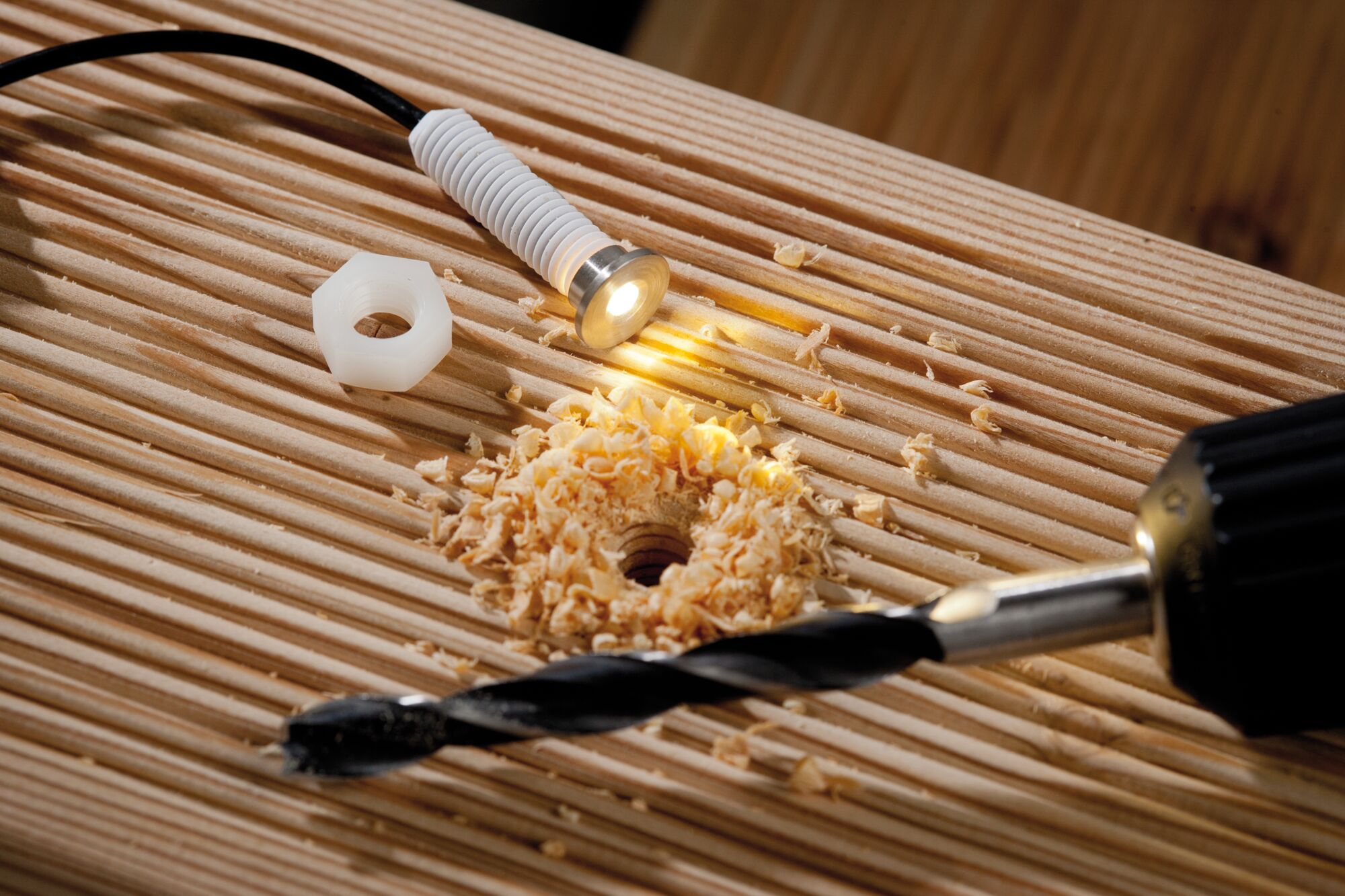 Kleine metalen LED-inbouwspot met witte kunststof schroefdraad op hout met boorsel en boor