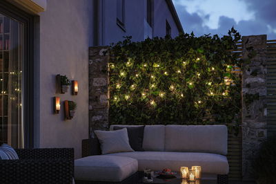 Hyggelig terrasse med grå polstret sofa, grøn plantevæg og varm hvide LED-lyskæder.