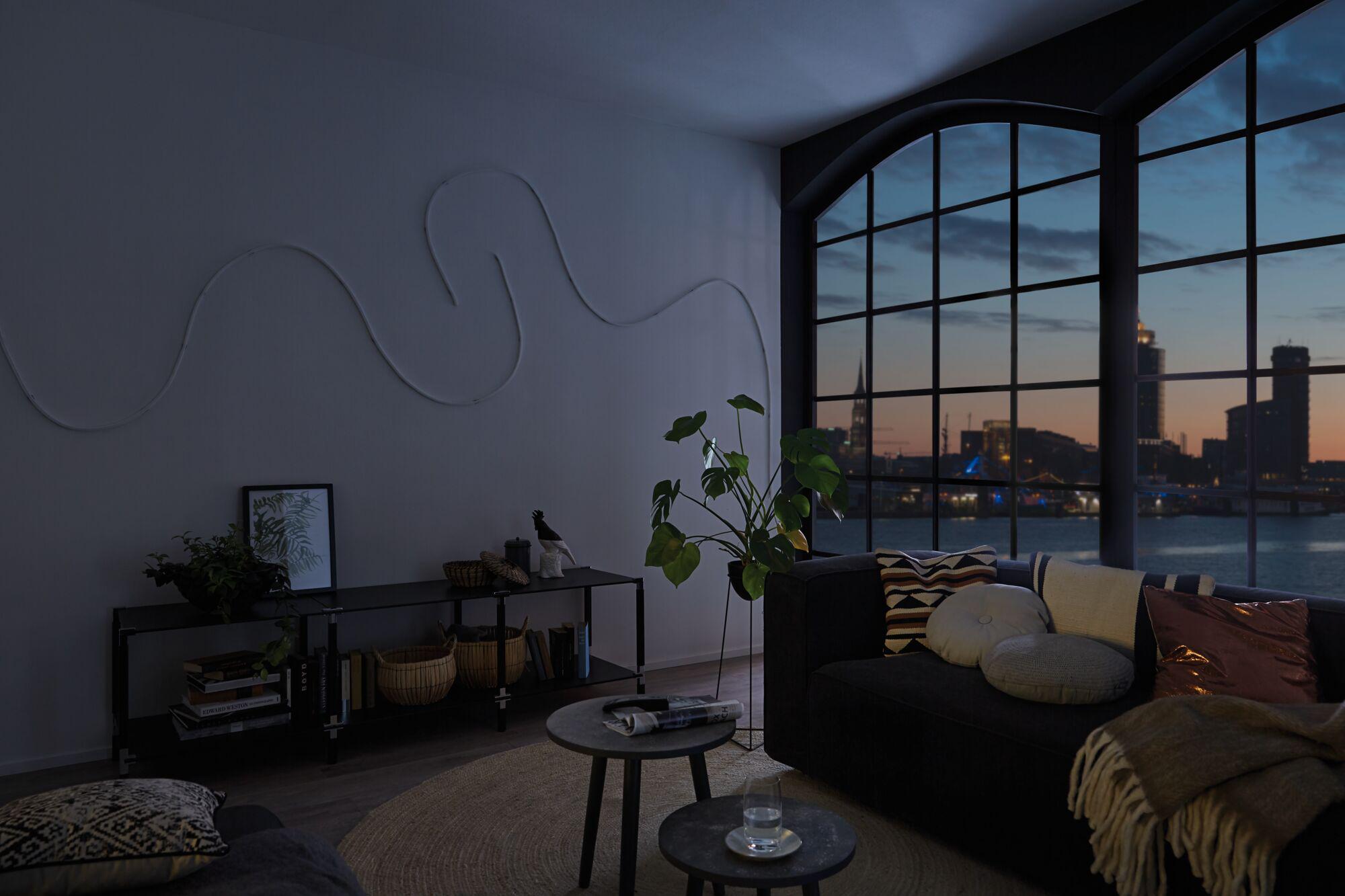 Modern living room with large windows and dark sofa, ambient LED lighting off at dusk.