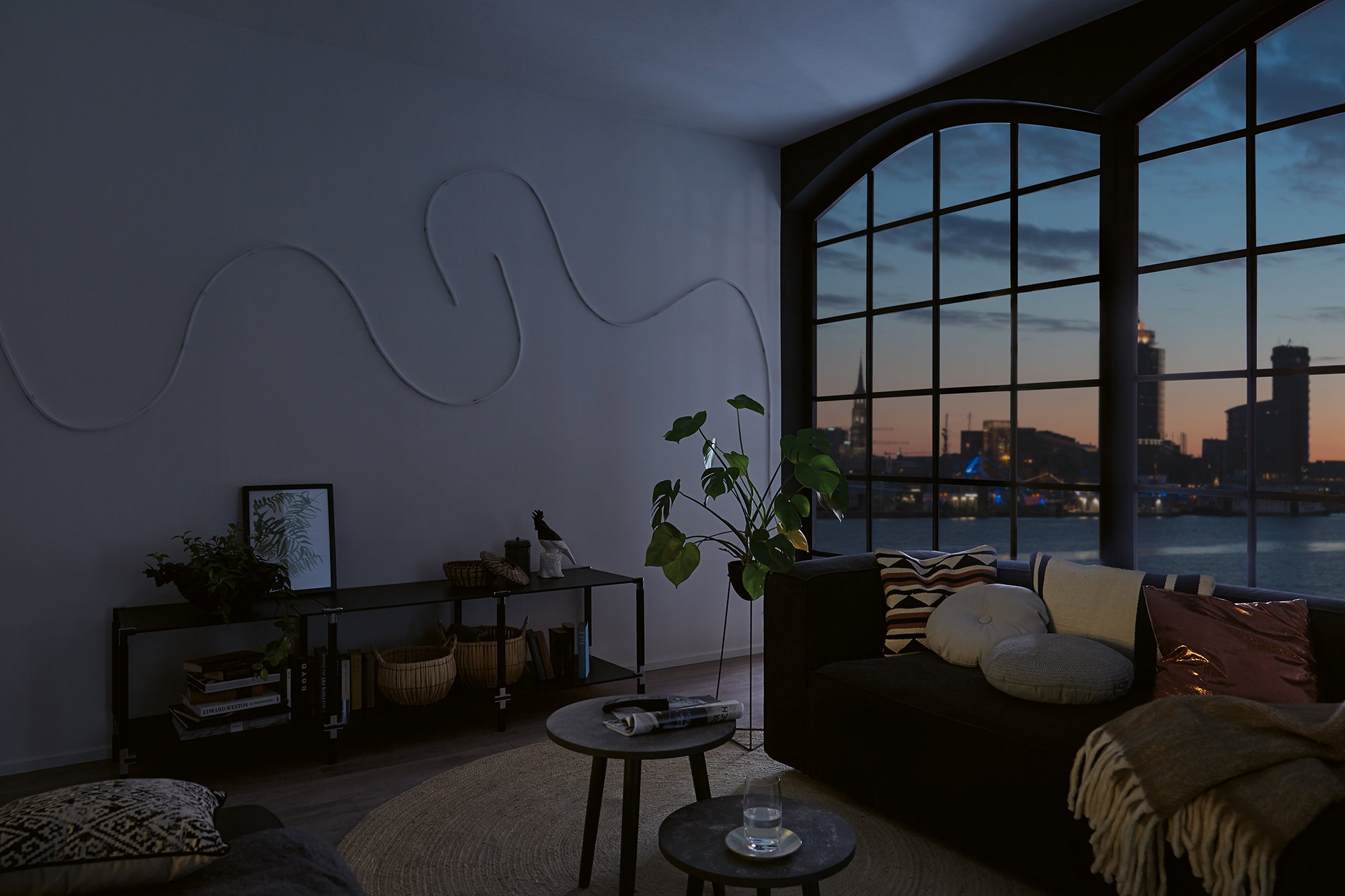 Dark living room with large window overlooking city at dusk without lighting