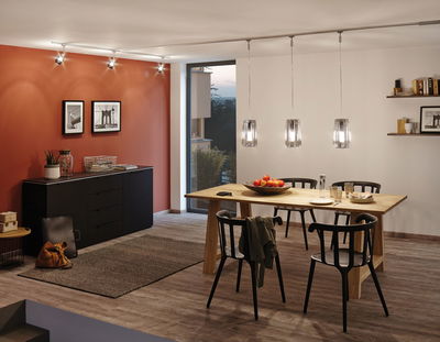 Moderne eetkamer met houten tafel, zwarte stoelen en drie hangende glazen hanglampen.