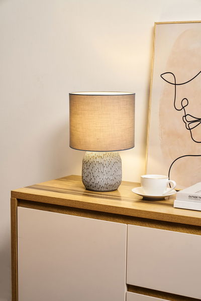 Table lamp with grey fabric shade and patterned ceramic base on wooden dresser in living room