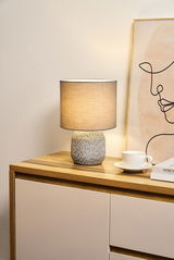 Lampe de table avec abat-jour en tissu gris et base en céramique à motifs sur commode en bois