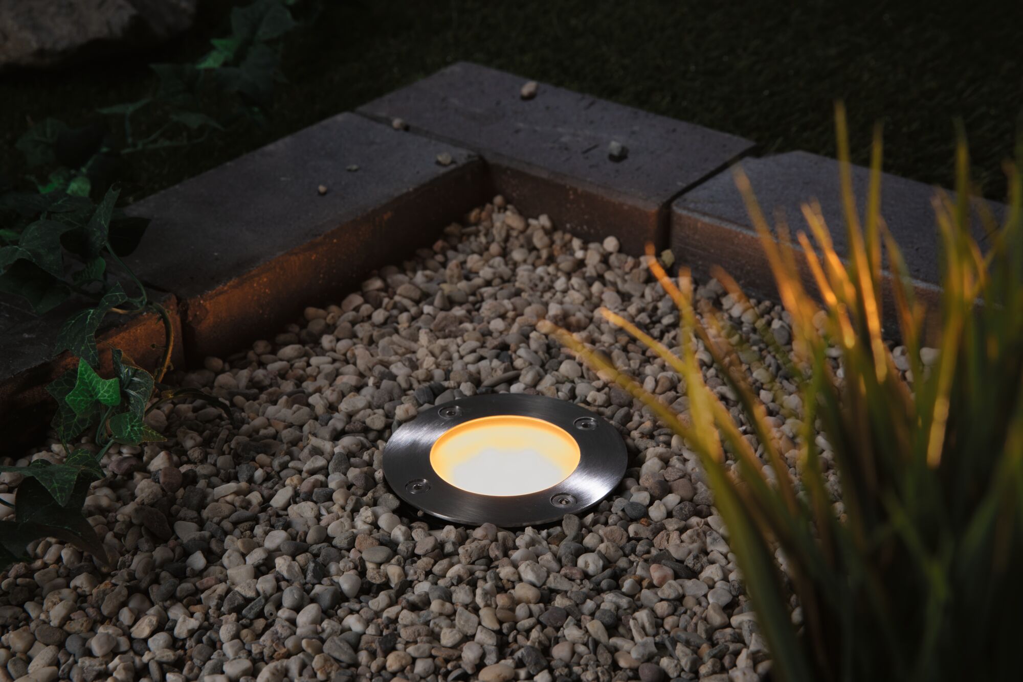 Recessed stainless steel LED floor light with warm white glow in gravel bed for garden lighting