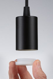Black cylindrical metal pendant light with white diffuser held by hand, modern LED lighting fixture