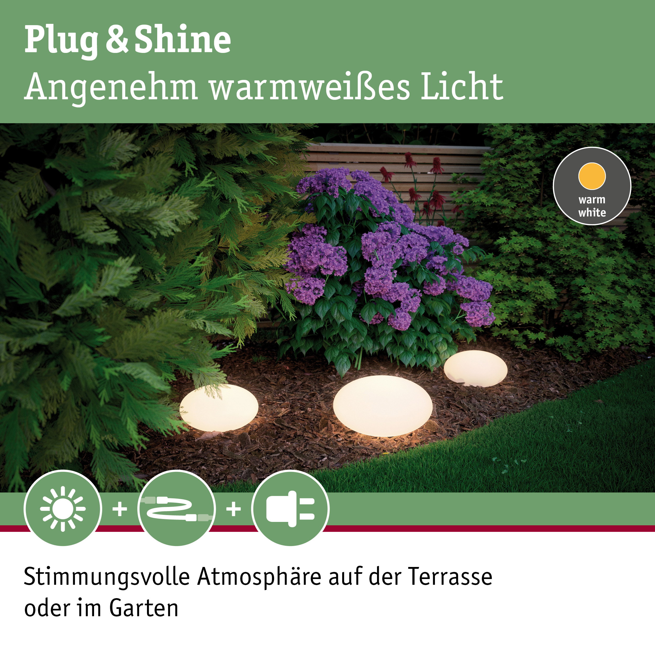 Drei kugelförmige Gartenleuchten mit warmweißem Licht auf Mulch neben lila Blüten und grünem Rasen