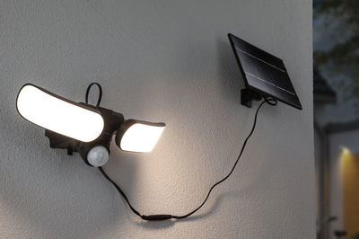 Black solar outdoor light with motion sensor and two bright LED panels mounted on white wall.