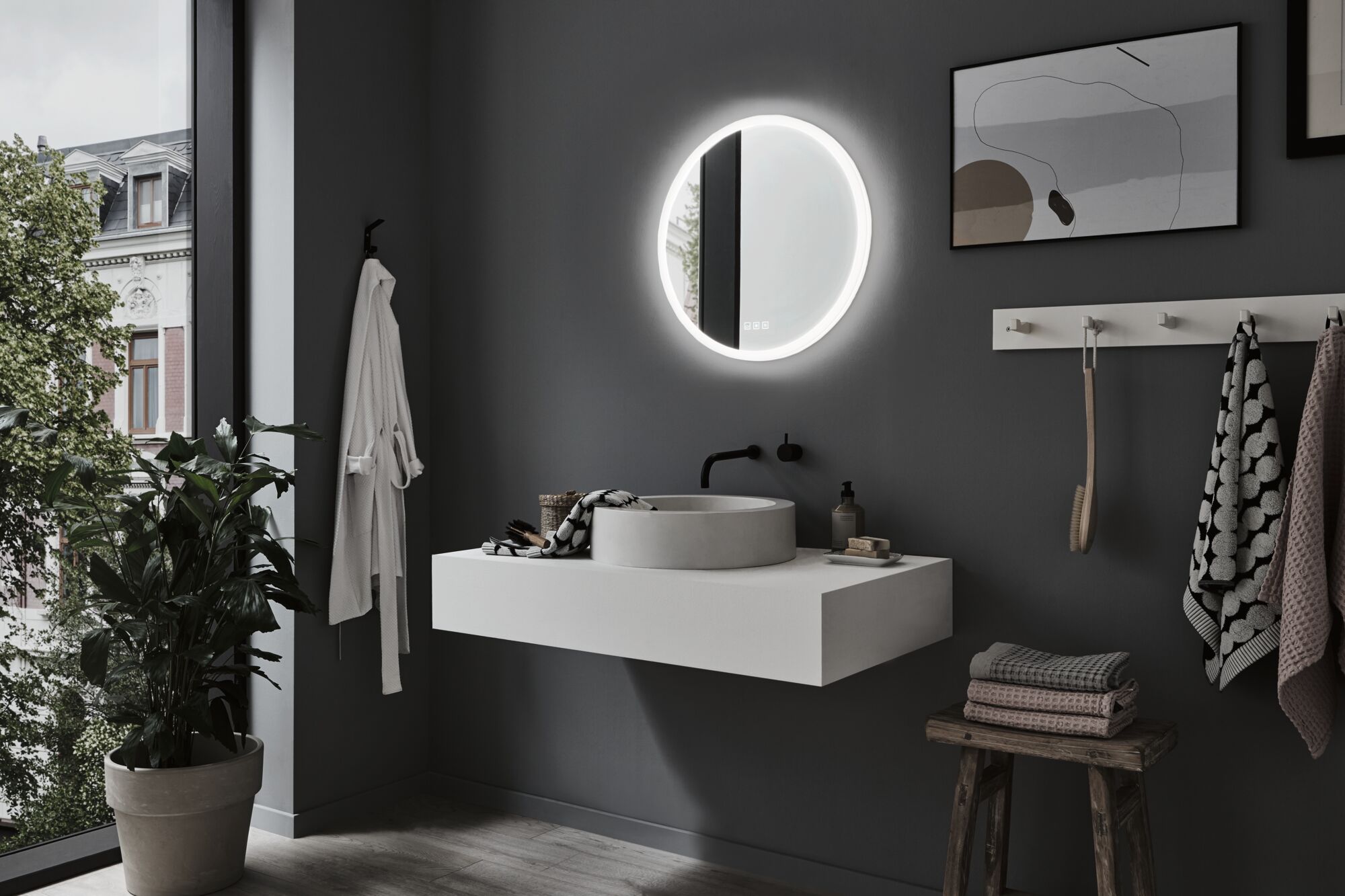 Modern bathroom with round LED mirror, grey wall, white sink, and wooden stool with towels