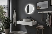 Round LED-lit bathroom mirror on grey wall above white basin in modern interior