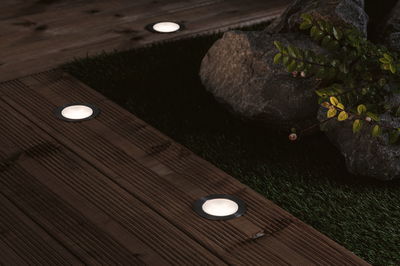 Round LED recessed floor lights with stainless steel frame on wooden terrace for garden lighting.