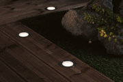 Runde LED-Bodeneinbauleuchten mit Edelstahlrahmen auf Holzterrasse für Gartenbeleuchtung.