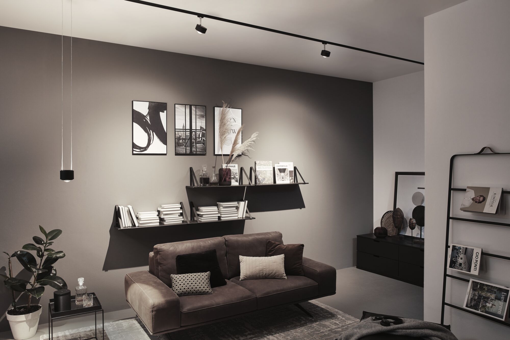 Salon moderne avec canapé en cuir marron, étagères murales noires et éclairage minimaliste au plafond