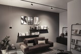 Salon moderne avec canapé en cuir marron, étagères murales noires et éclairage minimaliste au plafond