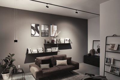 Salon moderne avec canapé en cuir marron, étagères murales noires et éclairage minimaliste au plafond