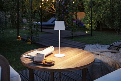 Lampe de table LED blanche avec abat-jour en tissu sur table en bois dans le jardin avec café et biscuits au crépuscule