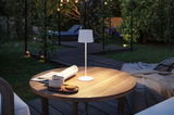 Lampe de table LED blanche avec abat-jour en tissu sur table en bois dans le jardin avec café et biscuits au crépuscule