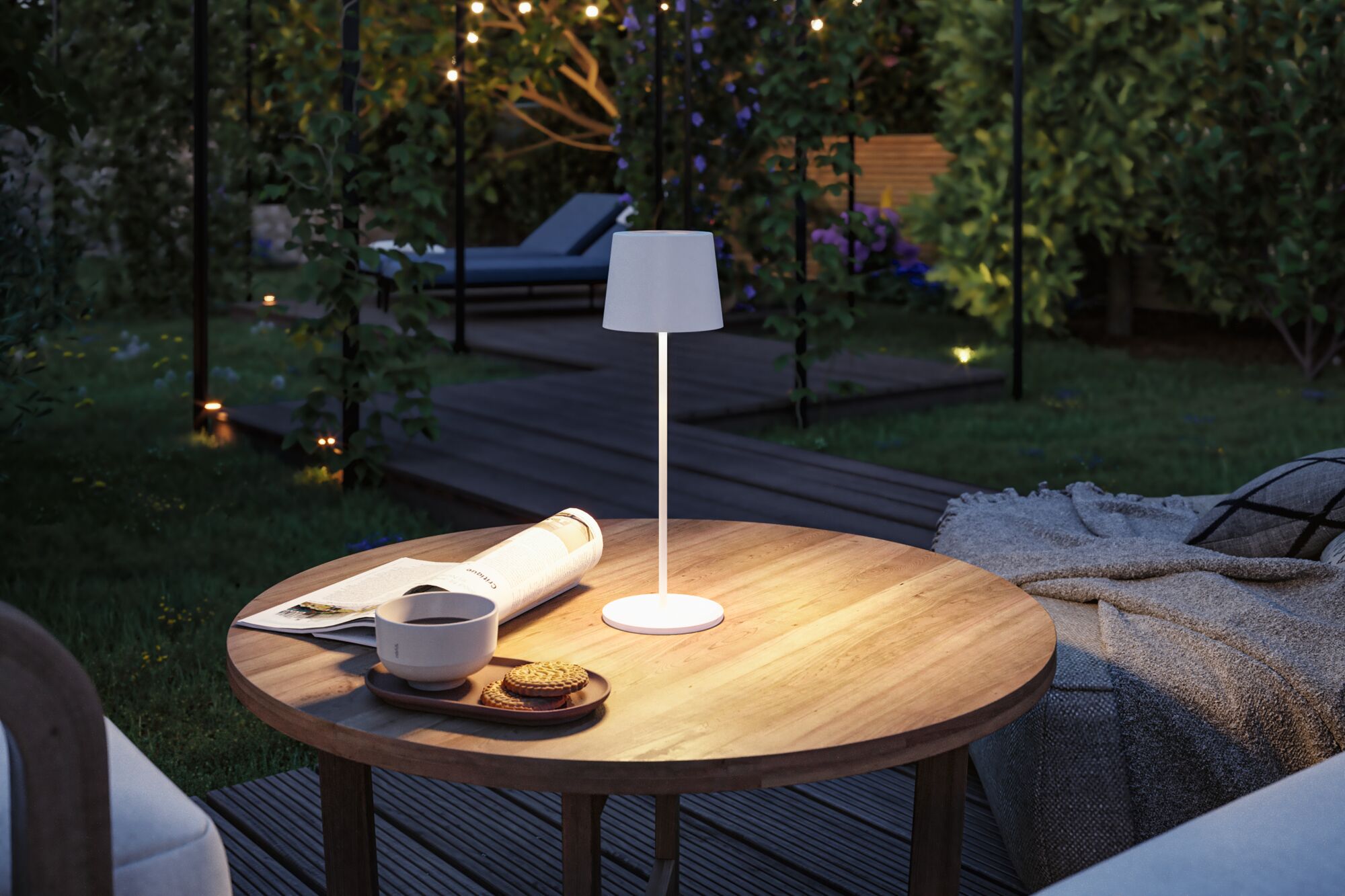 White LED table lamp with fabric shade on wooden garden table with coffee and cookies at dusk