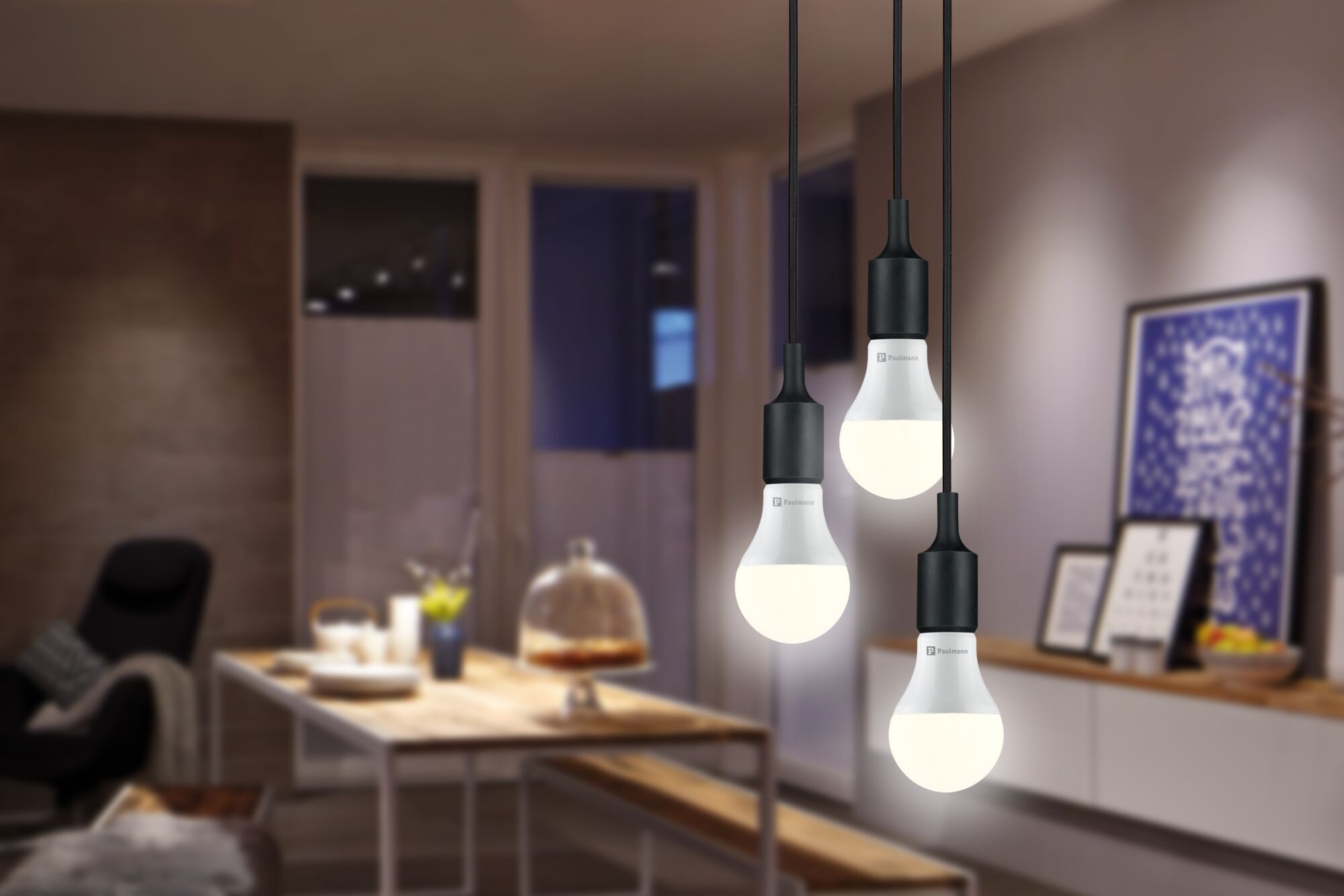 Trois suspensions LED blanches avec base noire dans une salle à manger moderne avec table en bois et décoration