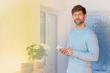 Man using white remote control for smart LED lighting in modern living room with plants