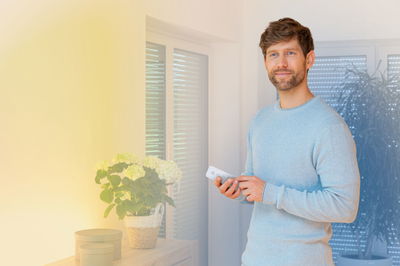 Mand styrer hvid fjernbetjening til smart LED-belysning i moderne stue med planter