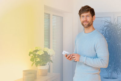 Mand styrer hvid fjernbetjening til smart LED-belysning i moderne stue med planter