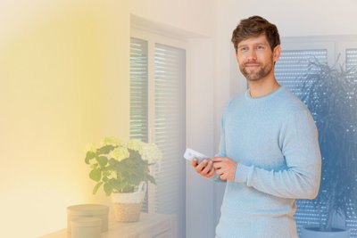 Man using white remote control for smart LED lighting in modern living room with plants