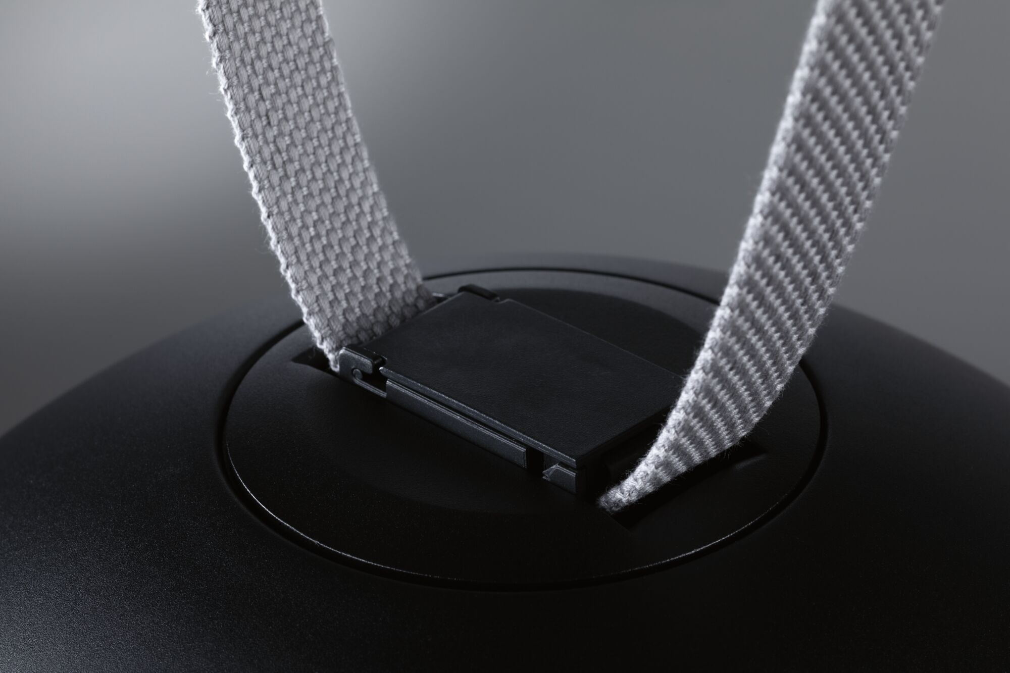 Nahaufnahme eines schwarzen Kunststoffclips mit grauem Textilband an einem technischen Gerät.