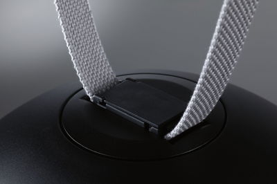 Nahaufnahme eines schwarzen Kunststoffclips mit grauem Textilband an einem technischen Gerät.