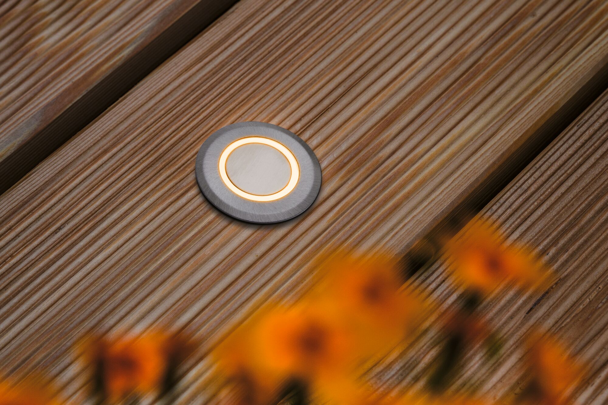 Round LED recessed floor light in brushed stainless steel with warm white light on wooden terrace