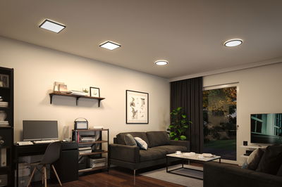 Modern living room with black furniture and square and round ceiling lights emitting warm white light