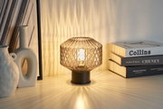 Table lamp with smoked glass and black metal base casting decorative light patterns on surface.