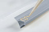 Grey plastic profile with beige sealant on white surface for sealing and installation use