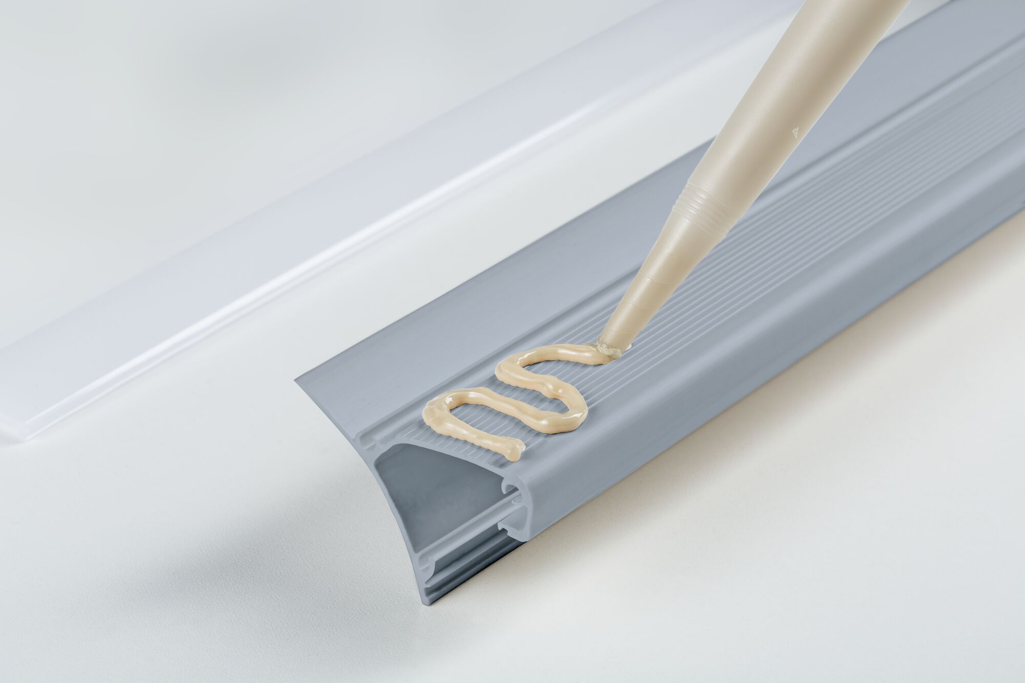 Graues Kunststoffprofil mit beige Dichtmasse auf weißem Untergrund für Abdichtung und Montage