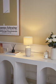 Weiße Keramik-Tischlampe mit strukturiertem Sockel und beigem Stoffschirm auf modernem Sideboard