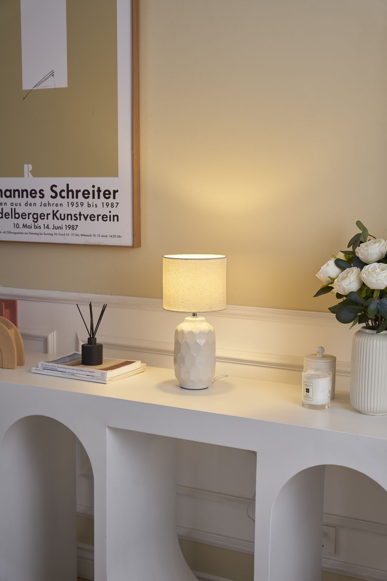 Weiße Keramik-Tischlampe mit strukturiertem Sockel und beigem Stoffschirm auf modernem Sideboard